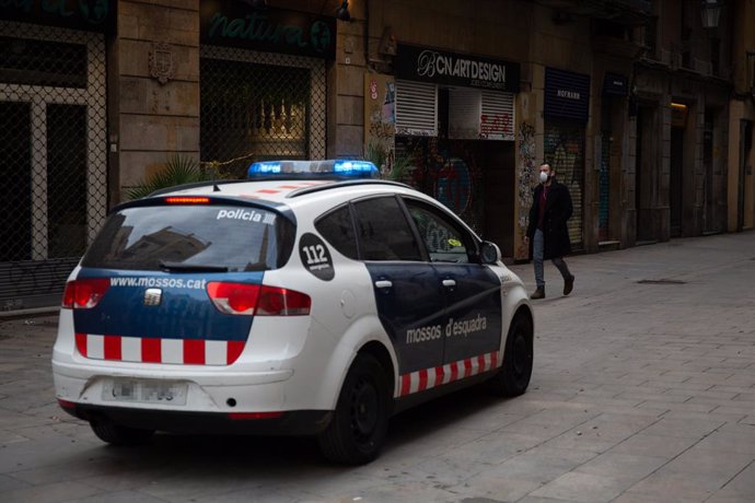 Un home amb mascarilla passeja per un carrer de Barcelona al costat d'un cotxe de la Policia en el segon dia laborable de l'estat d'alarma pel coronavirus, a Barcelona/Catalunya (Espanya), a 17 de mar de 2020.