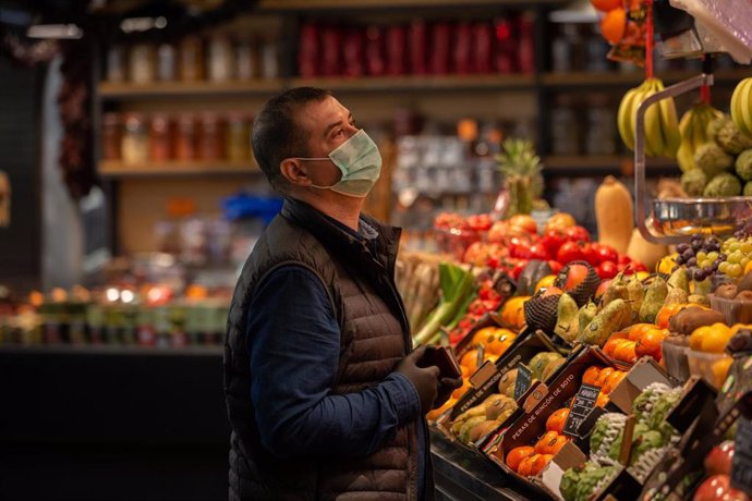 Un hombre protegido con mascarilla es atendido en una frutería durante el segundo día laborable del estado de alarma por el coronavirus, en Barcelona (España), a 17 de marzo de 2020.