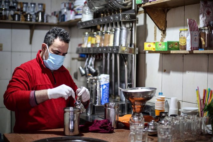 Una personas se protege con una mascarilla mientras prepara café en una cafetería de El Cairo.