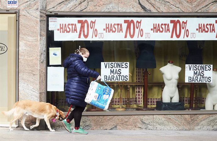 Una mujer con un paquete grande de papel higiénico pasea a su perro cerca de una tienda durante el tercer día laborable desde que se decreto el estado de alarma en el país a consecuencia del coronavirus, en Santander (Cantabria, España)