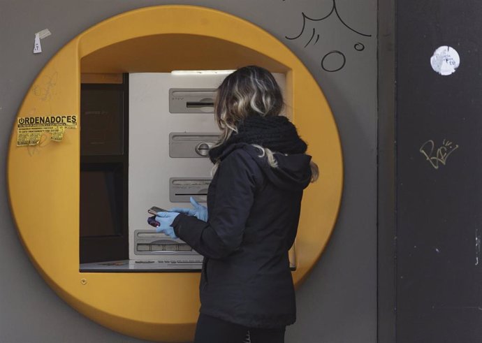 Una mujer saca dinero con guantes en el cajero de un banco durante el primer día laborable desde que se decretó el estado de alarma en todo el territorio nacional a consecuencia del coronavirus, en Alcorcón (Madrid), a 16 de marzo de 2020.