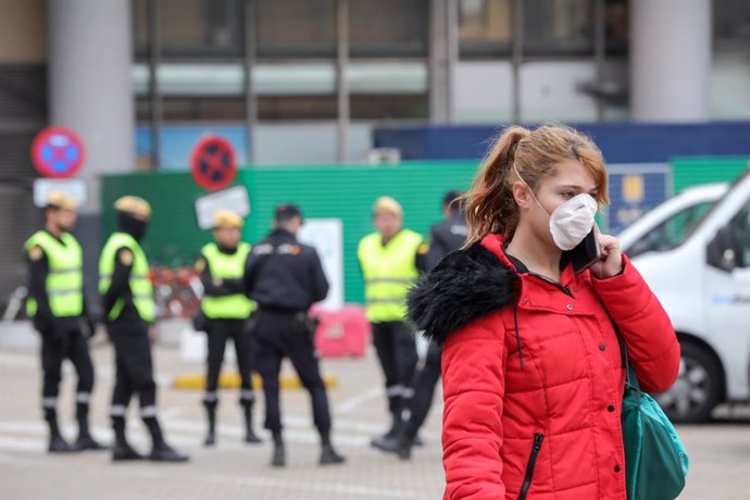 Una mujer con mascarilla circula cerca de donde se concentran efectivos de la Policía Nacional y del UME en las inmediaciones de la estación de tren Puerta de Atocha