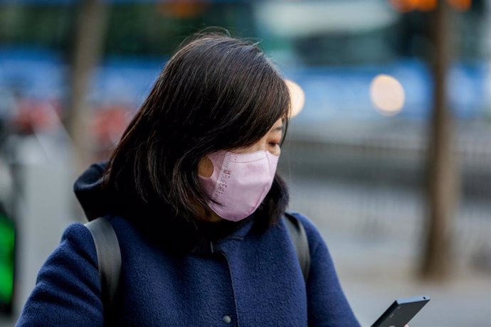 Una mujer asiática mira su móvil con una mascarilla protectora, mientras las farmacias registran una alta demanda de estas por parte de ciudadanos chinos tras el coronavirus, en Madrid (España), a 30 de enero.