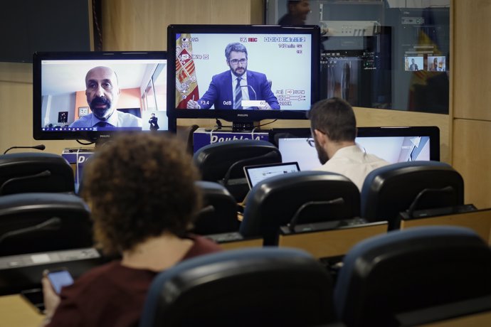 El ministro de Salud, Joan Martínez Benazet, desde su casa, y el ministro Portavoz, Eric Jover, en dos pantalas situadas en la sala de prensa del Gobierno.