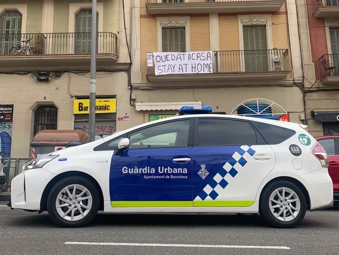Un cotxe de la Gurdia Urbana de Barcelona davant una pancarta amb el lema 'Queda't a casa' per la pandmia de coronavirus.