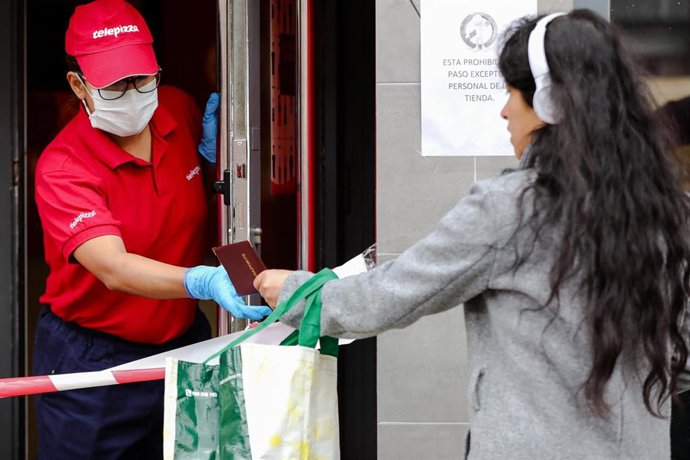 Una mujer entrega el Pasaporte a una trabajadora de Telepizza protegida con una mascarilla y unos guantes de látex, antes de recoger un menú infantil de Telepizza en el barrio de Abrantes