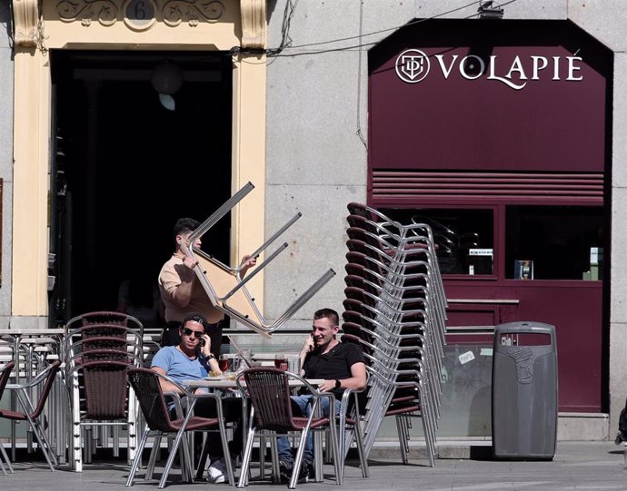 Dos hombres en una terraza de Madrid mientras un empleado recoge una de las mesas un día antes de que se cierre toda la hostelería para frenar contagios por coronavirus, en Madrid (España) a 13 de marzo de 2020.