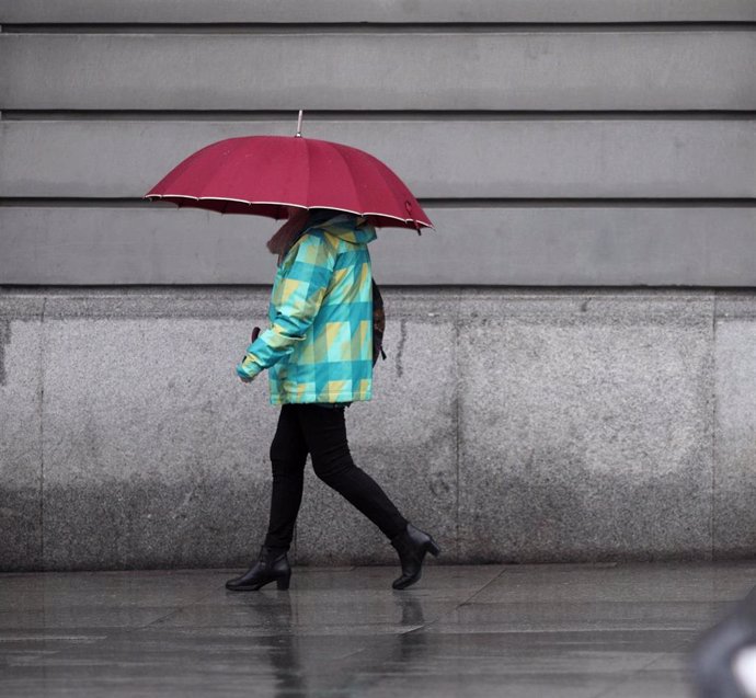 Una mujer pasea con paraguas en imagen de archivo
