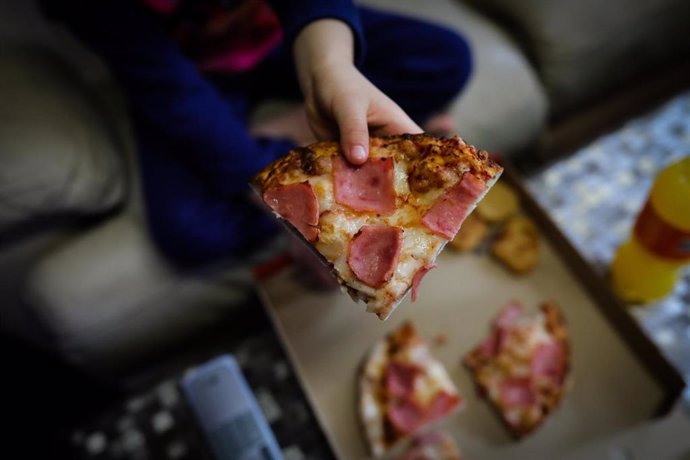 Un niño sostiene un trozo de pizza del menú infantil de Telepizza en el barrio de San Fermín en el distrito de Usera