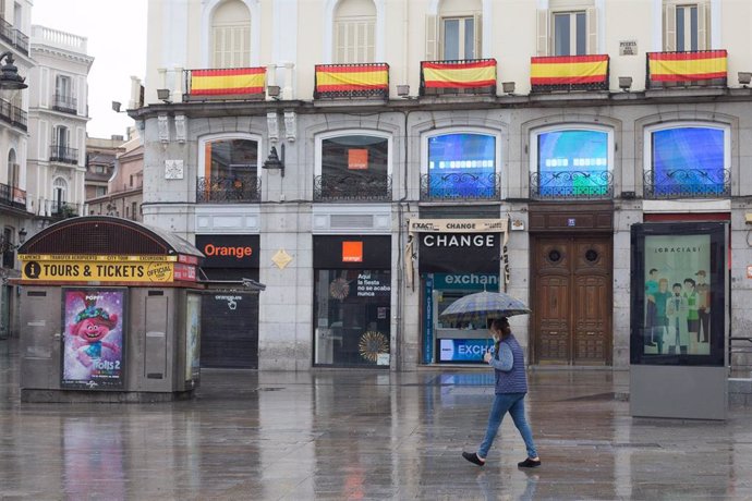 Una mujer protegida con mascarilla camina por la céntrica Puerta del Sol, prácticamente vacía durante el primer día laborable de la segunda semana desde que se decretó el estado de alarma en el país a consecuencia del coronavirus, en Madrid (España), a 