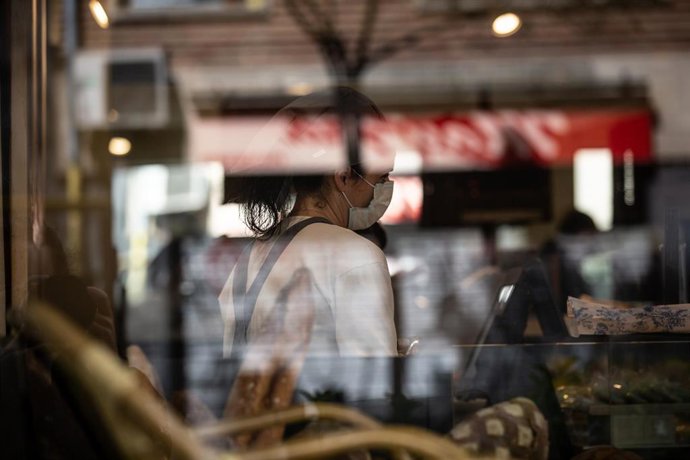 Una trabajadora atiende con una mascarilla protectora durante el primer día laborable de la segunda semana desde que se decretó el estado de alarma en el país a consecuencia del coronavirus, en Barcelona/Catalunya (España) a 23 de marzo de 2020.