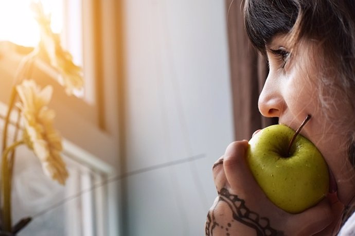 Comiendo una manzana mirando por la ventana melancólica.