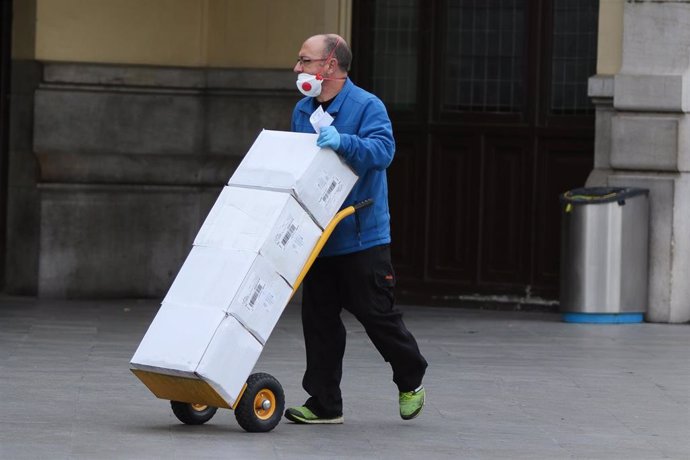 Un hombre con mascarilla y guantes carga con cajas.