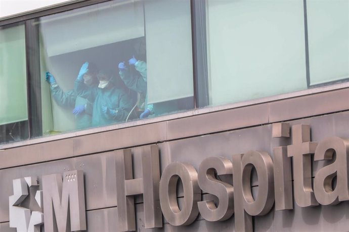 Sanitarios del Hospital de La Paz totalmente protegidos saludan desde una de las ventanas del centro 