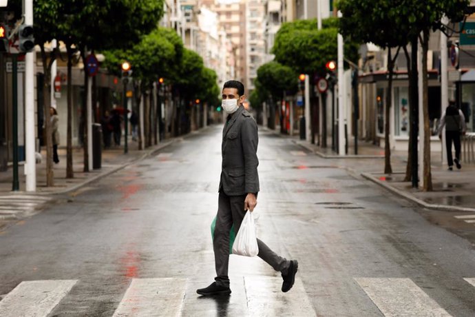 Una persona con mascarilla recorre la calle Alejandro Séiquer, vacía durante el estado de alarma, con bolsas de plástico en las manos, en Murcia (España) a 22 de marzo de 2020.
