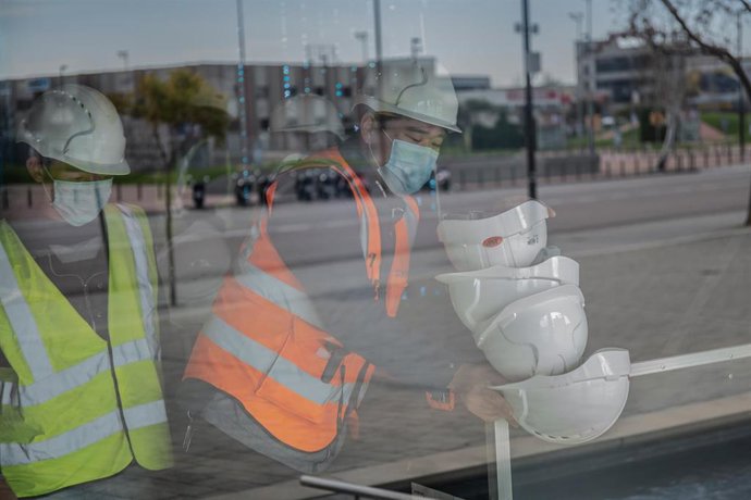 Dos trabajadores asiáticos colocan cascos blancos de obra en el pabellón del Mobile World Congress (MWC) durante el desmantelamiento de los stands de la feria, en Barcelona/Catalunya (España) a 13 de febrero de 2020.
