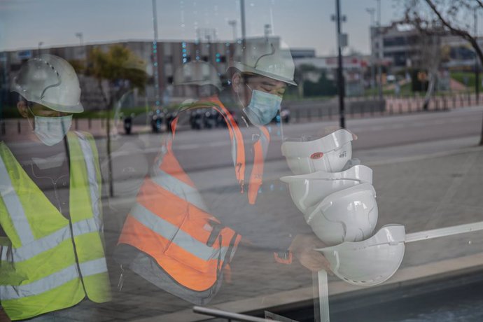 Dos treballadors asitics colloquen cascos blancs d'obra en el pavelló del Mobile World Congress (MWC) durant el desmantellament dels stands de la fira, a Barcelona/Catalunya (Espanya) a 13 de febrer de 2020.