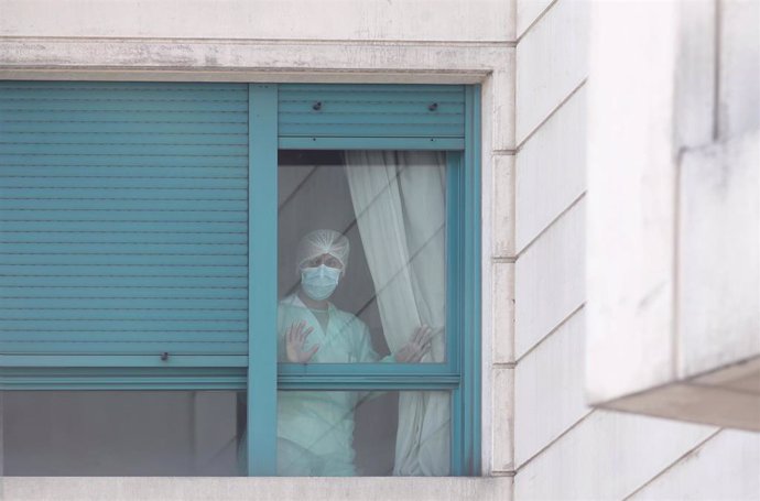 Una trabajadora del personal sanitario protegida con mascarilla se asoma por una de las ventanas de una residencia de Madrid.