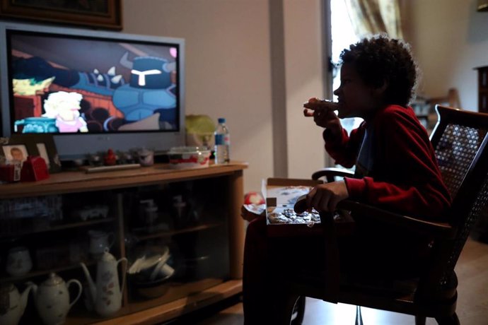 Un nen menja un tros de pizza mentre veu la televisió a la seva casa, a Madrid (Espanya) a 20 de mar de 2020.