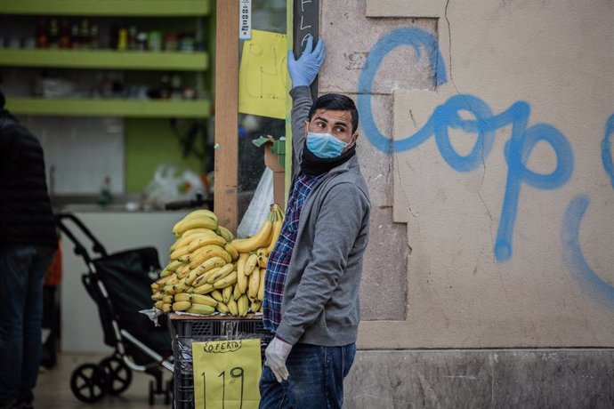 Un hombre protegido con mascarilla y guantes en la puerta de su establecimiento de alimentación en el barrio de El Raval, en Barcelona/Catalunya (España) a 23 de marzo de 2020.
