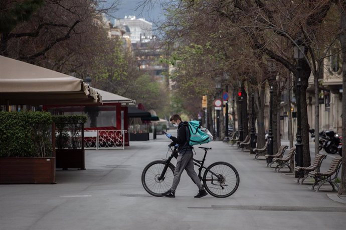 Un trabajador de Deliveroo en bicicleta por una calle de Barcelona, vacía durante el primer día laborable de la segunda semana desde que se decretó el estado de alarma en el país a consecuencia del coronavirus. 