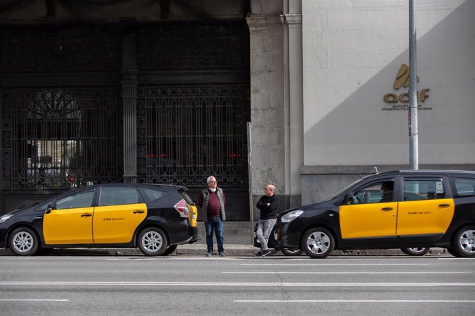 Dos taxistes esperen fora dels seus cotxes a recollir algun passatger en una estació de tren de Barcelona durant el tercer dia laborable de l'estat d'alarma per coronavirus, a Barcelona/Catalunya (Espanya) a 18 de mar de 2020.