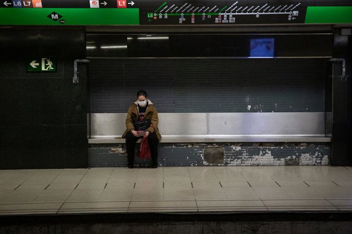 Una mujer protegida con mascarilla espera sentada en un banco del andén a que llegue el metro durante el estado de alarma