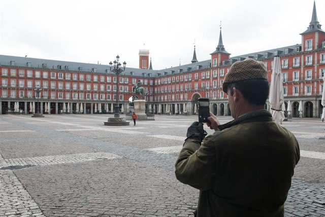 Un hombre hace una foto con su móvil a la céntrica Plaza Mayor de Madrid vacía 