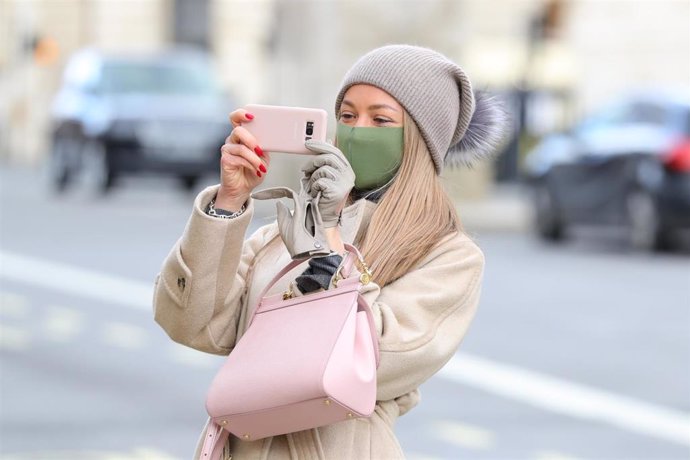 Una mujer hace una foto con su smartphone en Londres mientras lleva una mascarilla durante el brote de coronavirus