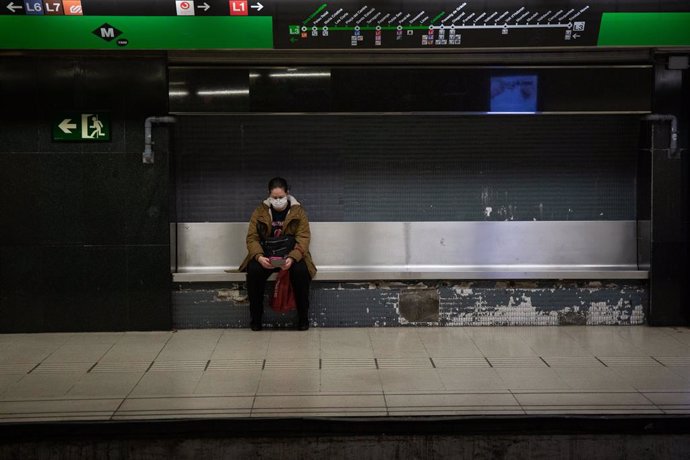 Una dona protegida amb mascarilla espera asseguda en un banc de l'andana al fet que arribi el metre durant l'estat d'alarma