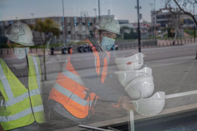 Dos trabajadores asiáticos colocan cascos blancos de obra en el pabellón del Mobile World Congress (MWC) durante el desmantelamiento de los stands de la feria tras la cancelación de la misma