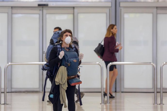 Una mujer protegida con mascarilla recoge su equipaje de la Terminal 4 del Aeropuerto Adolfo Suárez-Madrid Barajas 