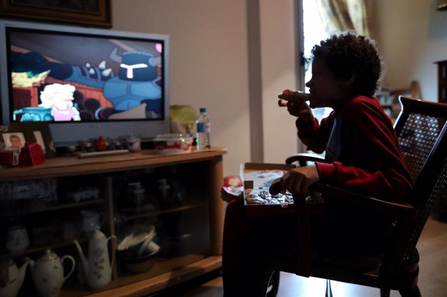 Un niño come un trozo de pizza mientras ve la televisión en su casa de Madrid durante el confinamiento.