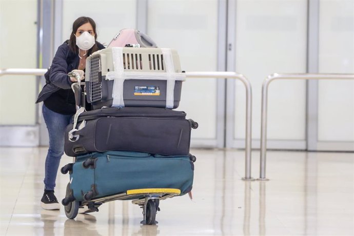 Una mujer protegida con mascarilla recoge su equipaje de la Terminal 4 del Aeropuerto Adolfo Suárez-Madrid Barajas