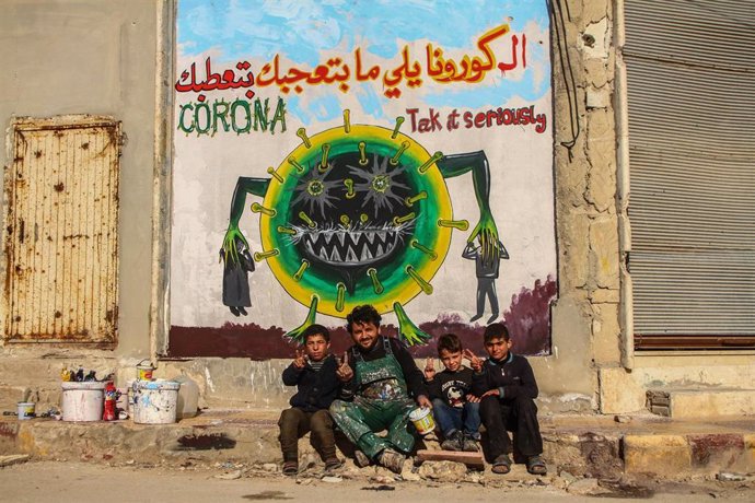 Un combatiente y varios niños frente a un mural que advierte del riesgo del coronavirus en Siria