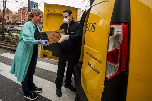 Una trabajadora sanitaria de la Clínica Ruber recoge las pizzas que le ha llevado un repartidor de Correos.