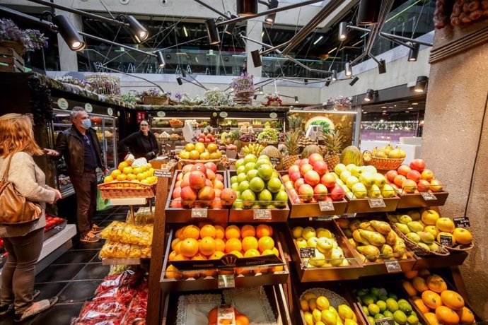 Varios clientes con mascarilla hacen la compra en un puesto de fruta en el mercado de San Antón, que permanece abierto en plena crisis del coronavirus y anuncia que también atiende a domicilio, en Madrid (España).