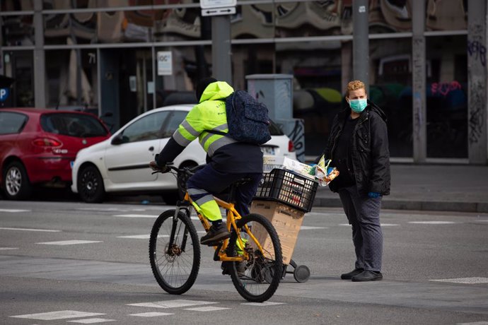 Un home que munta amb bicicleta passa al costat d'una dona protegida amb una mascarilla durant el nov dia laborable des que es va decretar l'estat d'alarma al país a conseqüncia del coronavirus, a Barcelona/Catalunya (Espanya) a 26 de mar de 2020.