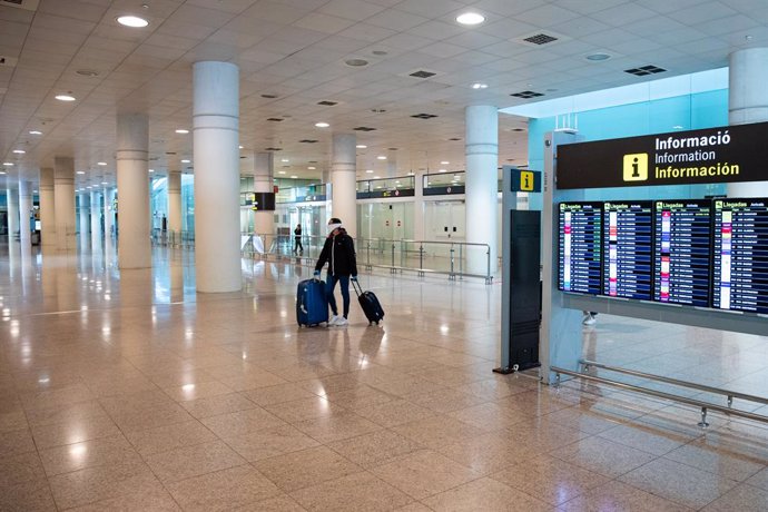Un pasajero  pasa por delante de los paneles del aeropuerto El Prat de Barcelona  