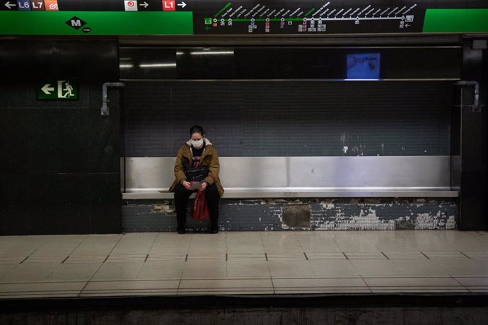 Una mujer protegida con mascarilla espera sentada en un banco del andén a que llegue el metro, durante el noveno día laborable desde que se decretó el estado de alarma a consecuencia del coronavirus, en Barcelona/Catalunya (España) a 26 de marzo de 2020.