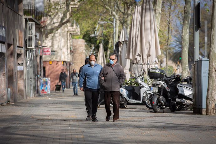 Dos homes protegits amb mascarillas caminen per un carrer durant el nov dia laborable des que es va decretar l'estat d'alarma al país a conseqüncia del coronavirus, a Barcelona/Catalunya (Espanya) a 26 de mar de 2020.