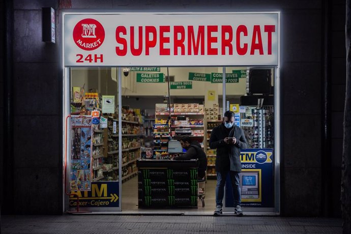 Un hombre protegido con una mascarilla en la puerta de un supermercado 24 horas durante el primer día laborable de la segunda semana desde que se decretó el estado de alarma por el coronavirus, en Barcelona/Catalunya (España) a 23 de marzo de 2020.