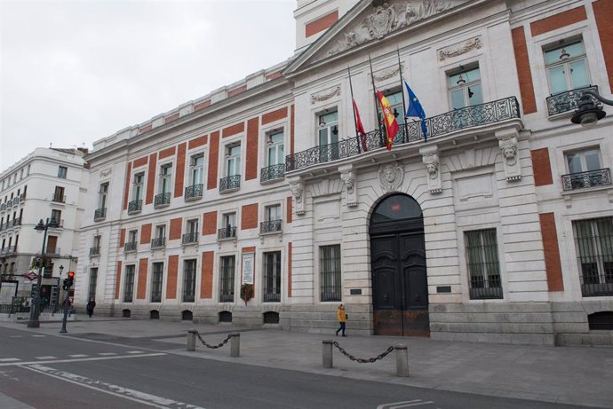 Fachada del la Real Casa de Correos, sede de la Comunidad de Madrid, con las banderas a medio asta durante el minuto de silencio en el primer día del luto oficial por los fallecidos del COVID-19.