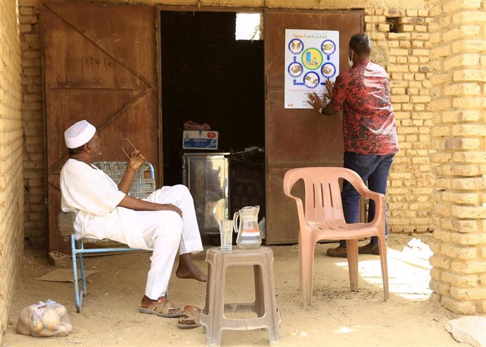 Sudaneses frente a un cartel informativo sobre las medidas de protección ante la pandemia de coronavirus