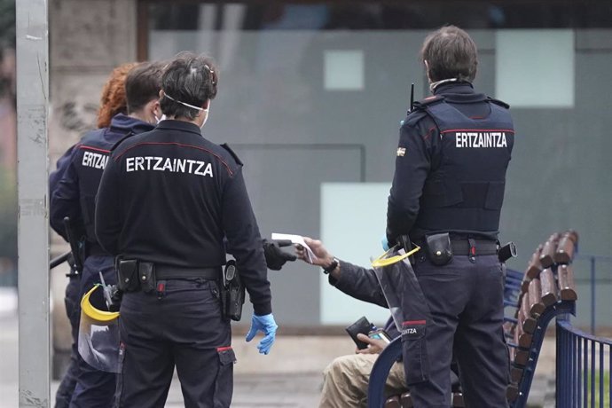 Efectivos de la Ertzaintza le piden la documentación a una persona que se encontraba en un banco en pleno estado de alarma por coronavirus donde los movimientos están restringidos, en Bilbao, País Vasco, (España), a 31 de marzo de 2020.