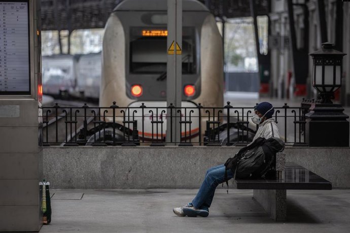 Un home protegit amb una mascareta espera assegut en un banc en una estació de tren de Barcelona durant el segon dia laborable de l'estat d'alarma pel coronavirus, a Barcelona (Espanya), a 17 de mar de 2020.
