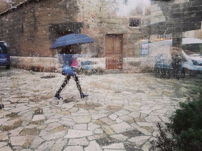 Una mujer pasea por el centro de Palma con un paraguas, vista a través de un cristal con gotas de lluvia en una imagen de archivo