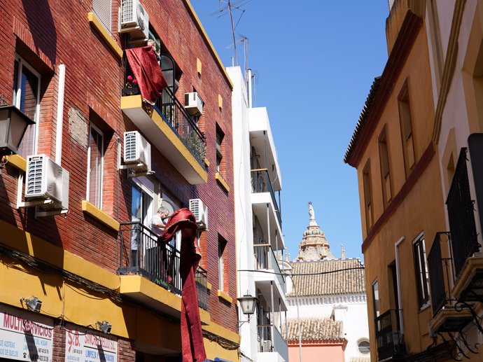 Vecinos de la Calle Santiago del barrio del centro de Sevilla  adornan su balcón con colgaduras  en vísperas de Semana Santa.
