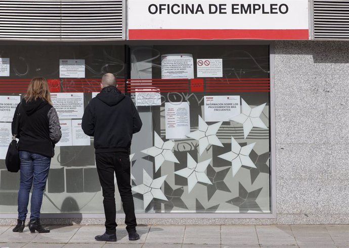 Dos personas leen los carteles de una oficina de empleo cerrada durante el primer día laborable desde que se decretó el estado de alarma