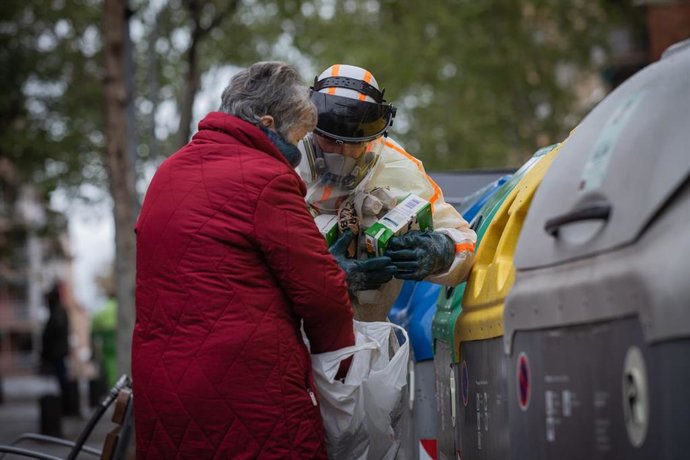 Un trabajador que desinfecta y limpia los contenedores de basura de Barcelona ayuda a una mujer durante la tercera semana de confinamiento por la crisis del coronavirus. (archivo)